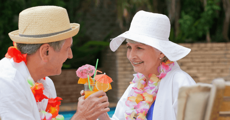 Senior couple sitting by the pool toasting their umbrella drinks