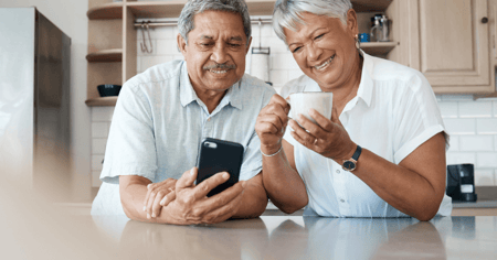 Elder man with cell phone in hand and elder woman drinking coffee in active adult retirement living.