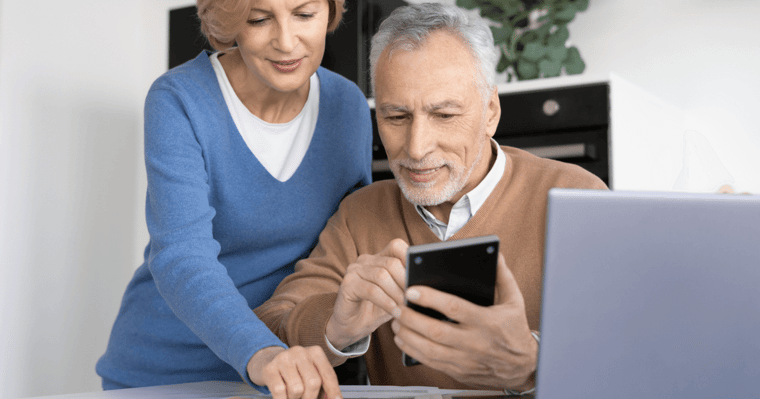 Older man on phone with older woman leaning over him