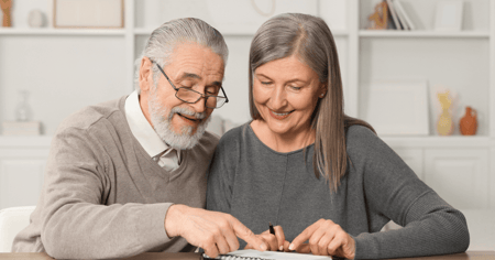 Senior couple sitting at the table reviewing the cost of home to senior living on paper.