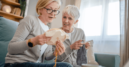 Adult daughter crocheting with mother in retirement community 