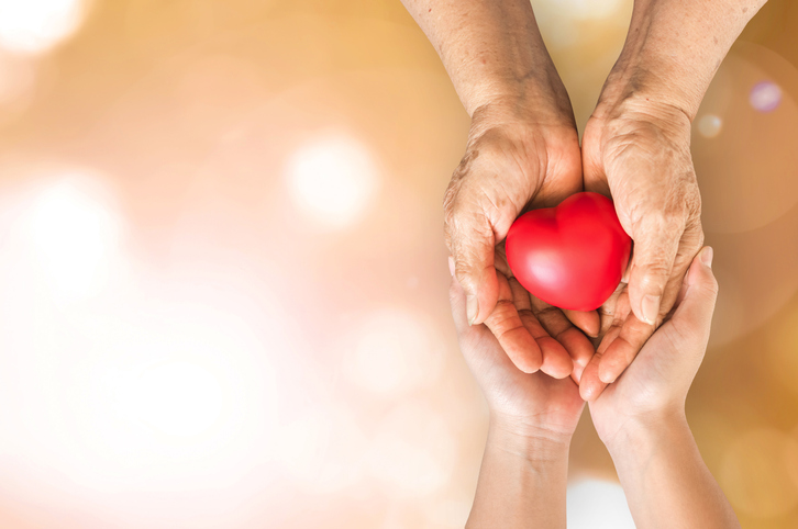 Caregiver holding the hands of their aging loved one holding a heart