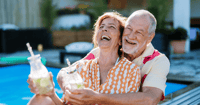 Elder couple hugging by pool with drinks in independent living