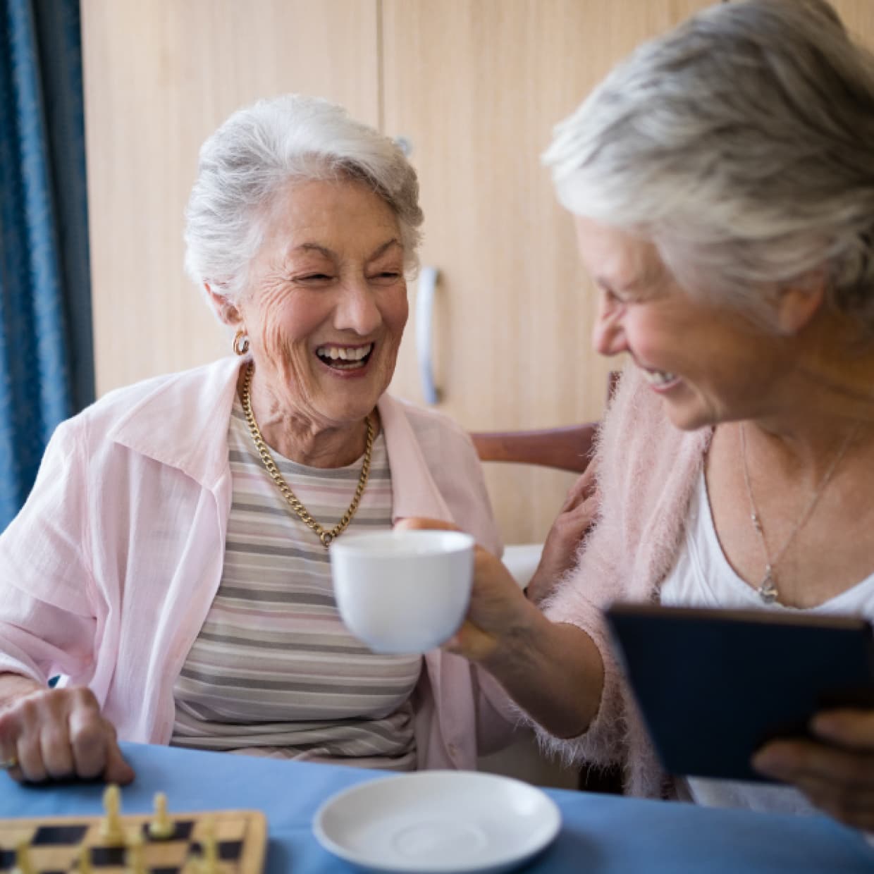 Two women laughing while enjoying breakfast and chess together. 
